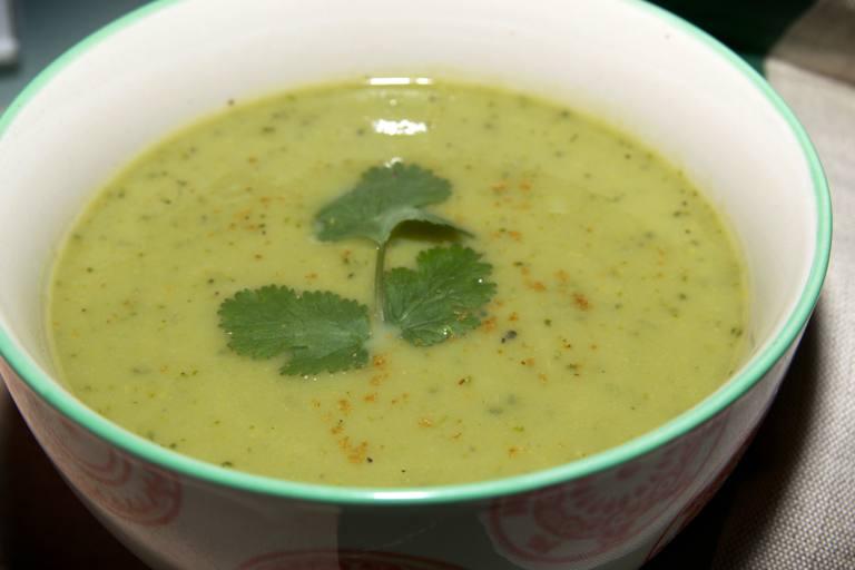 Sopa de berros con una ramita de cilantro como guarnición en un tazón blanco con borde verde.